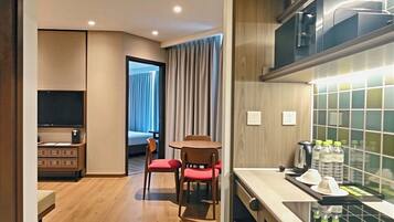 A compact hotel room with a kitchenette, wooden flooring, a dining area with chairs, and a view through a door.