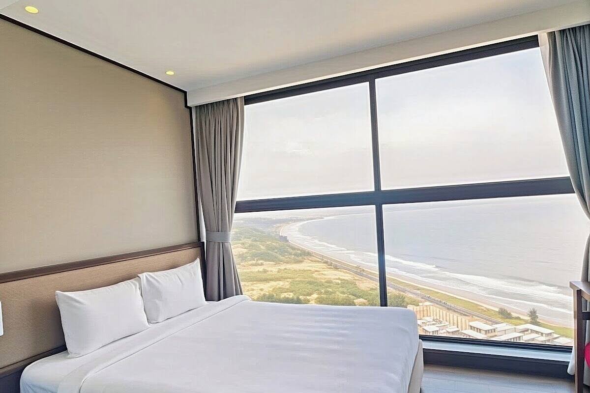 Une chambre d’hôtel moderne avec un grand lit, une vue sur la plage et une grande fenêtre.