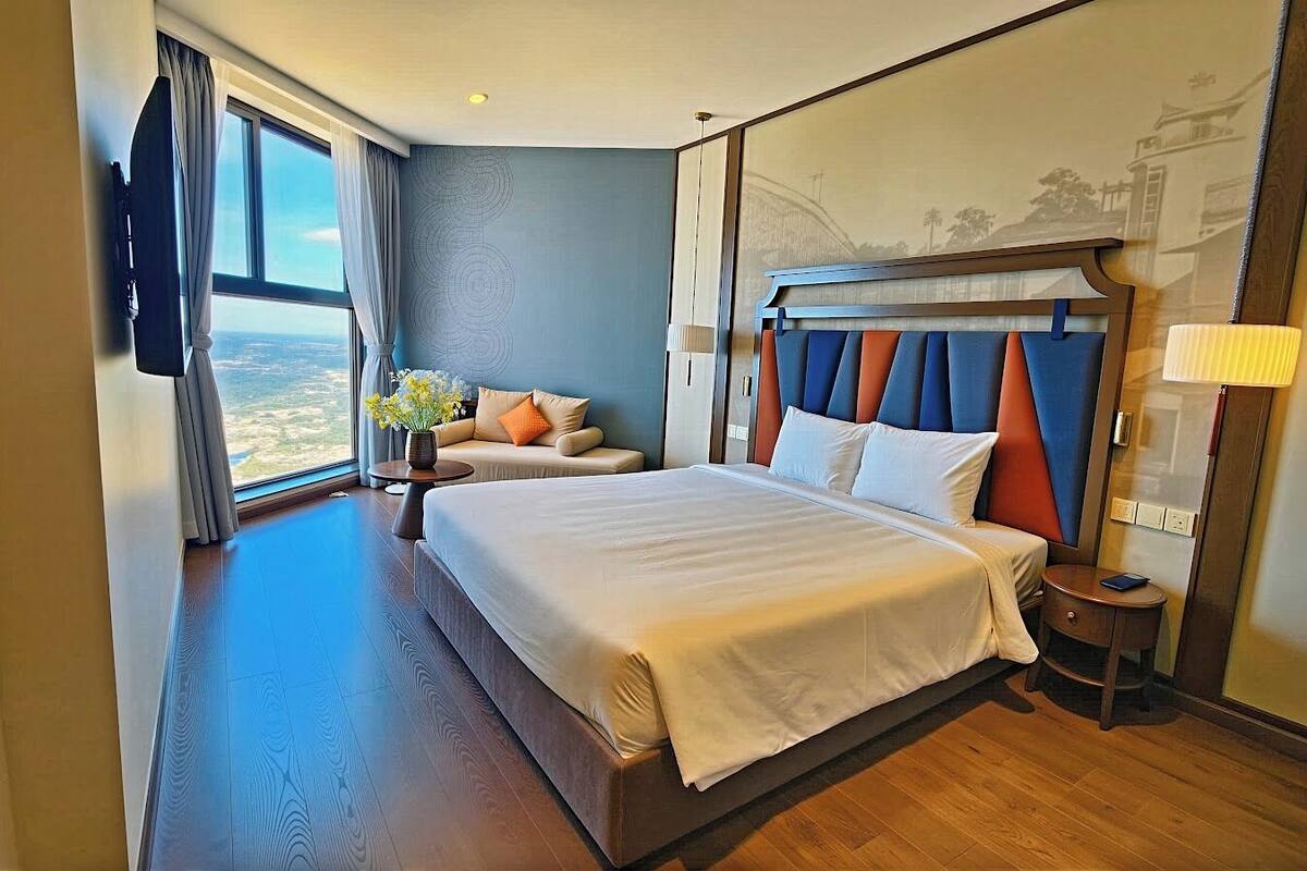 Une chambre d’hôtel avec un grand lit, un canapé, une petite table ornée de fleurs et une vue sur la ville.