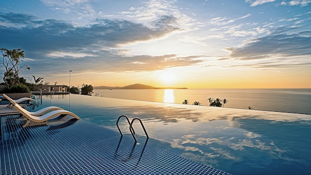 An infinity pool with a view of the sunset over the ocean, lounge chairs, and palm trees. - Apec Mandala Mũi Né Resorts & Hotels NN (Mui Ne)