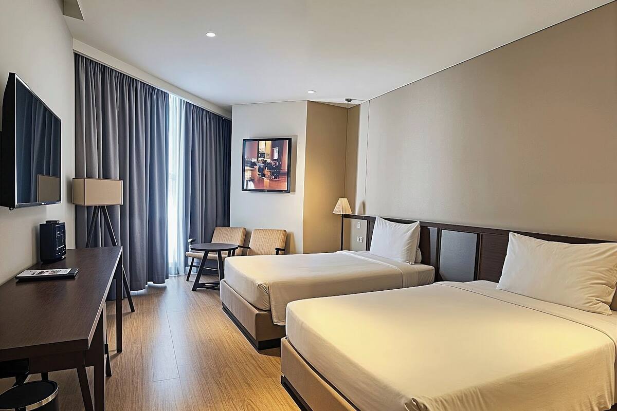 Une chambre d’hôtel avec deux lits, un bureau avec un ordinateur, une télévision et un tableau au mur.
