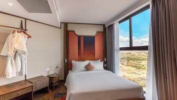 Ein Hotelzimmer mit einem großen Bett, einer hölzernen Bank, einem Bademantelständer und Blick auf die Wüste durch das Fenster.