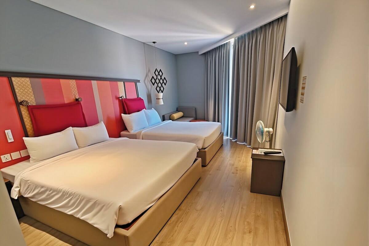 Une chambre d’hôtel avec deux lits, une télévision, une table de chevet et une fenêtre avec des rideaux.