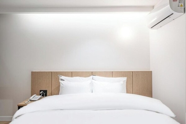 Una habitación de hotel con cabecera de madera, cama blanca y teléfono junto a la cama.