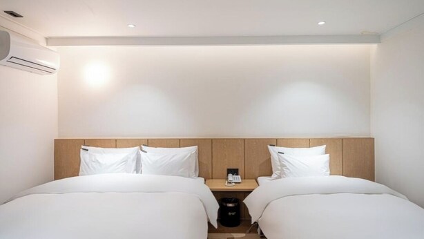 A hotel room with two beds, a wooden headboard, a bedside table with a phone, and an air conditioning unit. - Brown Dot Hotel NamGumi (Chilgok)