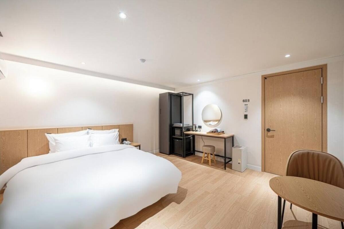 A modern hotel room with a large bed, a desk with a computer, a chair, and a wardrobe.