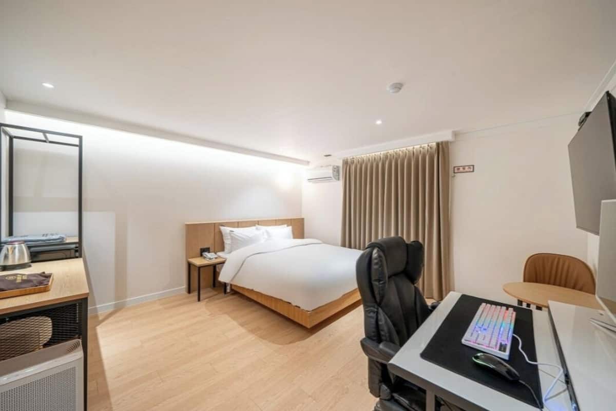 A modern hotel room with a bed, desk, chair, and a flat-screen TV.