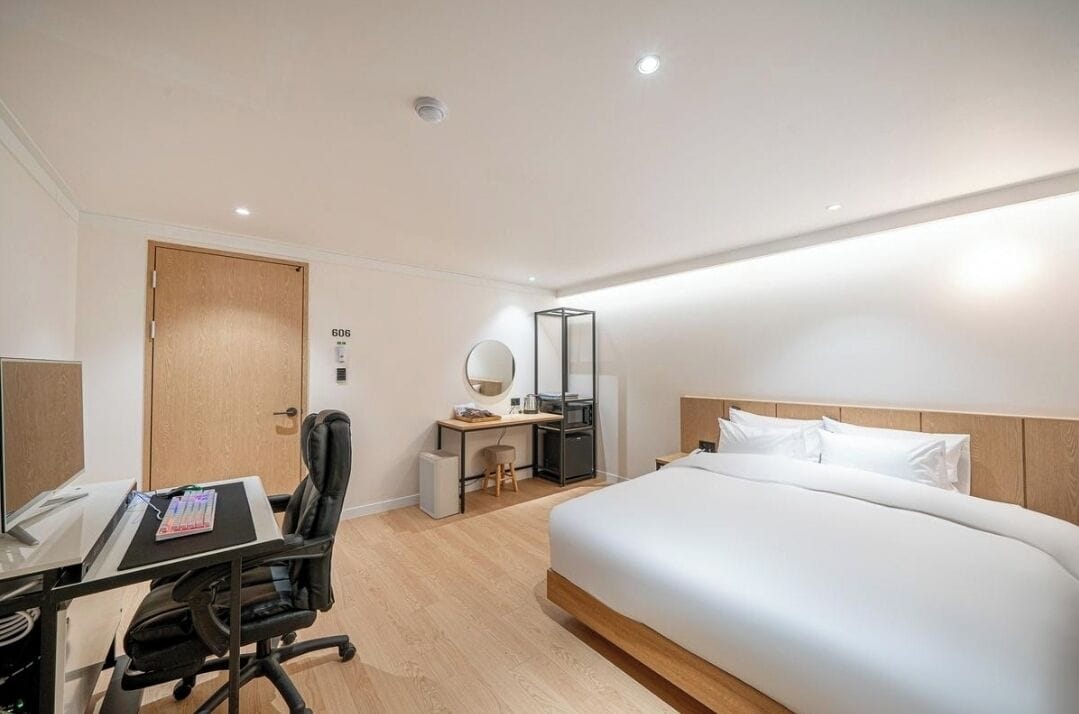 A hotel room with a bed, desk, chair, and a small table with a mirror.