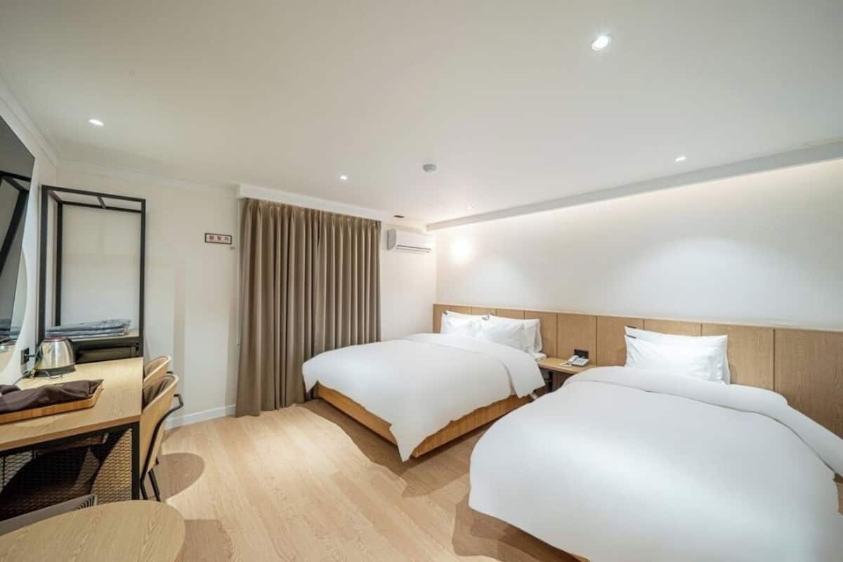 A hotel room with two beds, a desk, a chair, and a mirror.