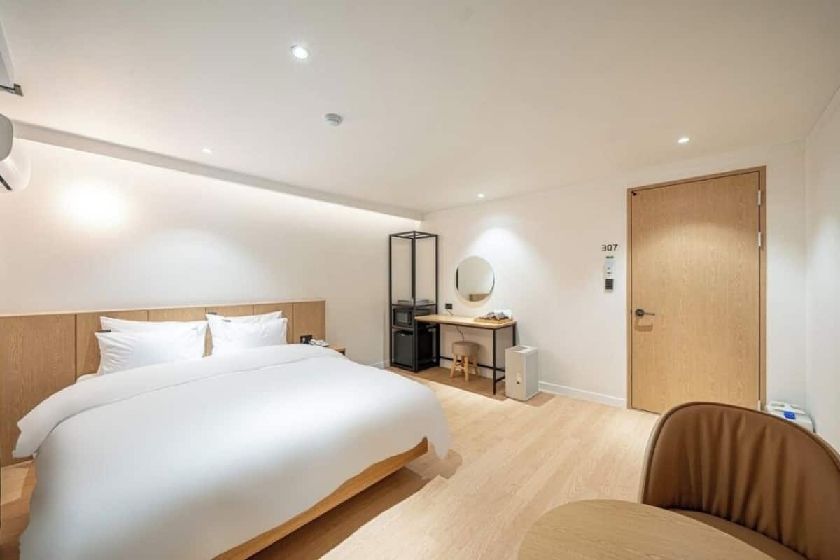 A modern hotel room with a large bed, a desk with a chair, a wardrobe, and a door marked with the number 307.