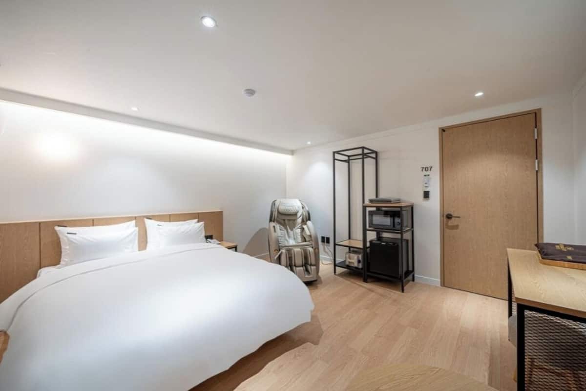 A modern hotel room with a large bed, a massage chair, a small desk, and a door marked with the number 707.