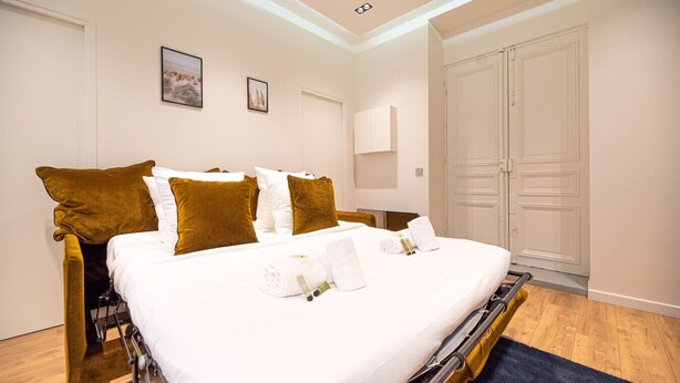A hotel room with a bed, a wardrobe, and a bedside table.