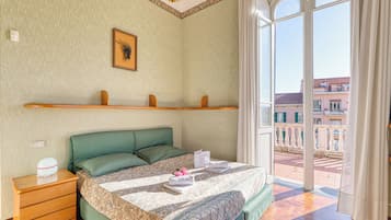 Una habitación de hotel con cama, mesita de noche, ventana con vistas a edificios e iluminación decorativa en el techo.