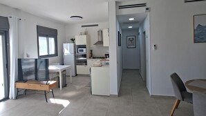 Ein modernes Wohnzimmer mit Fernseher, Sitzgelegenheiten und einer Küche im Hintergrund.