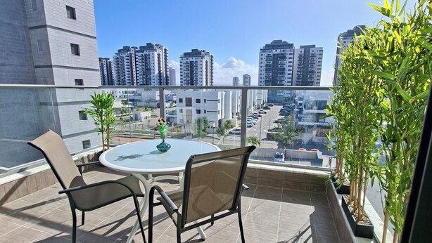 Ein Balkon mit Tisch und Stühlen, einem Blumentopf und Blick auf hohe Gebäude.