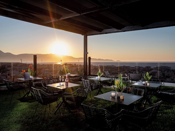An outdoor seating area with tables and chairs, a bottle of wine, and a vase of flowers.