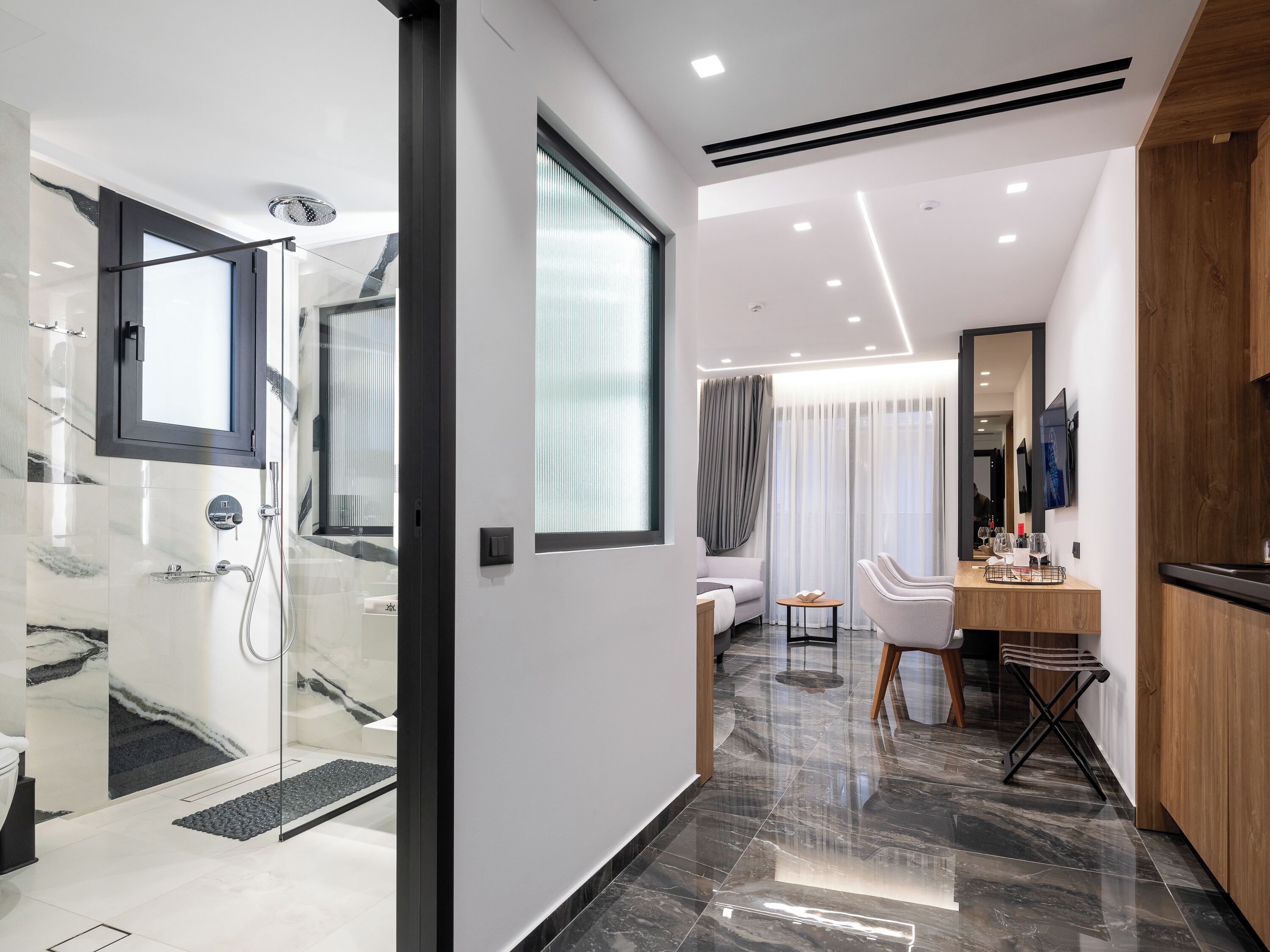 A modern bathroom with a glass shower enclosure, a vanity with a mirror, and a seating area with a sofa and chairs.