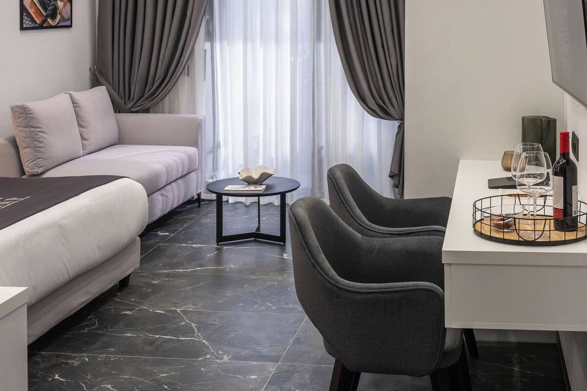 Une chambre d’hôtel moderne équipée d’un canapé, d’une table à manger avec des chaises, d’une télévision et d’une grande fenêtre avec des rideaux.