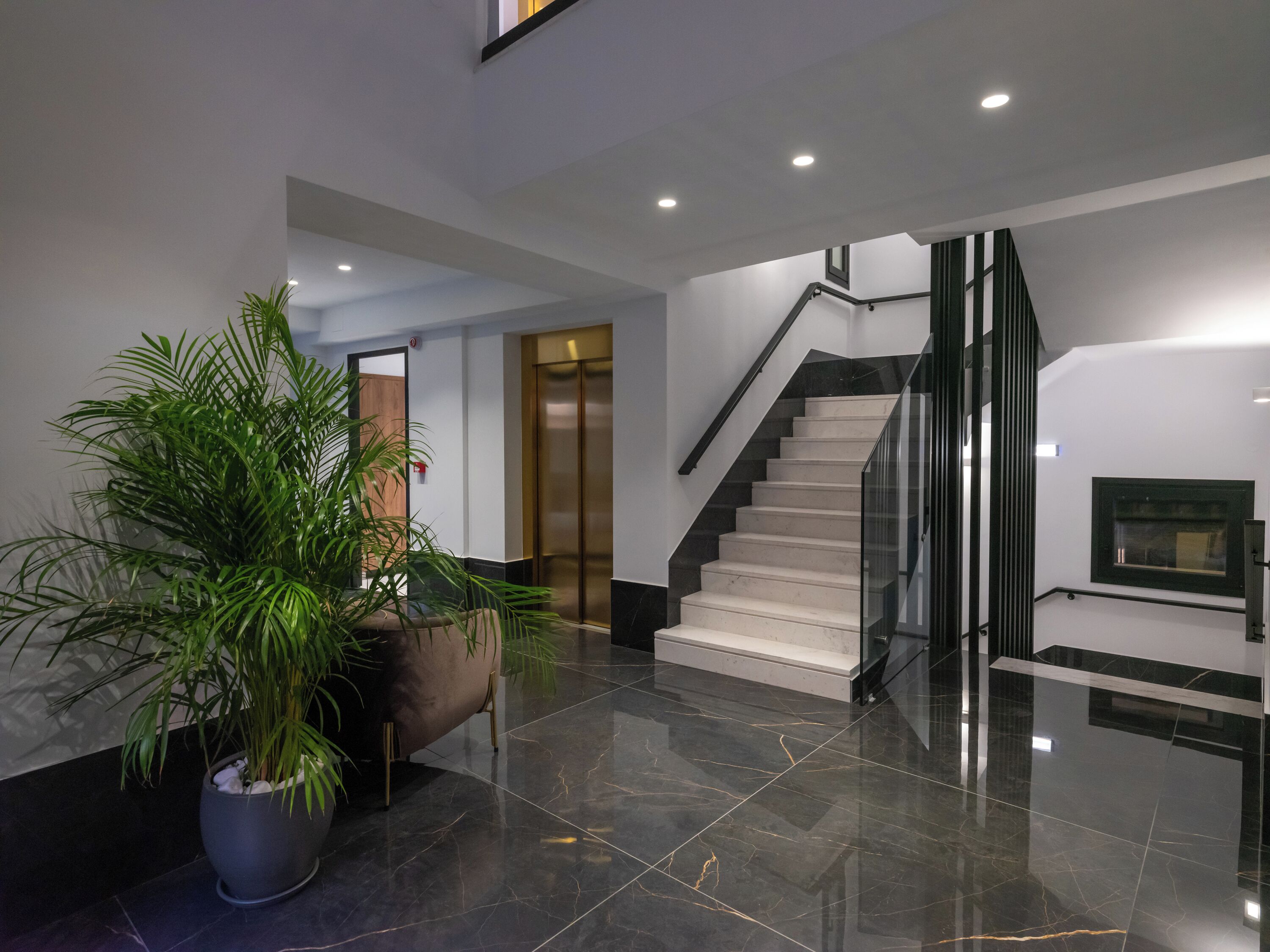 A modern interior with a marble floor, a staircase, and a large potted plant.