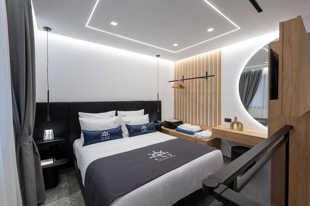 Une chambre d’hôtel moderne avec un lit bien fait, un bureau en bois, un miroir et un petit coin salon.