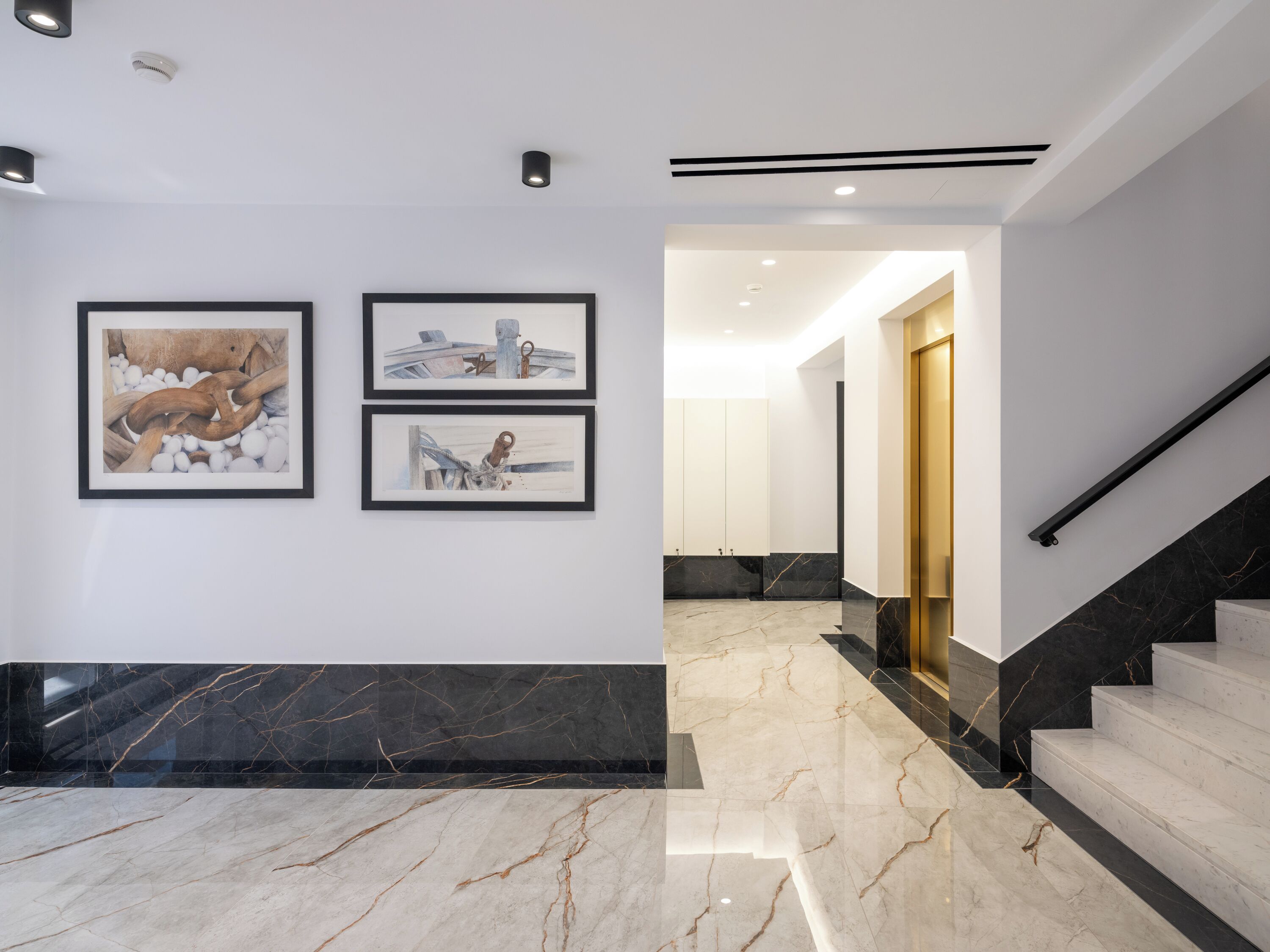 Ein modernes Interieur mit Marmorböden, gerahmten Kunstwerken und einer Treppe mit schwarzer Handlauf.