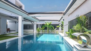 Un área de piscina moderna con una piscina azul cristalina, rodeada de paredes blancas y plantas verdes.