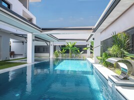 A modern pool area with a clear blue pool, surrounded by white walls and green plants.