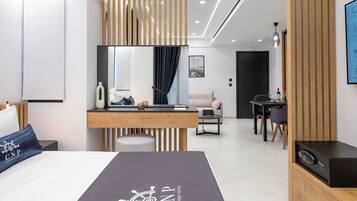 A modern hotel room with a bed, a desk, a sofa, and a TV.