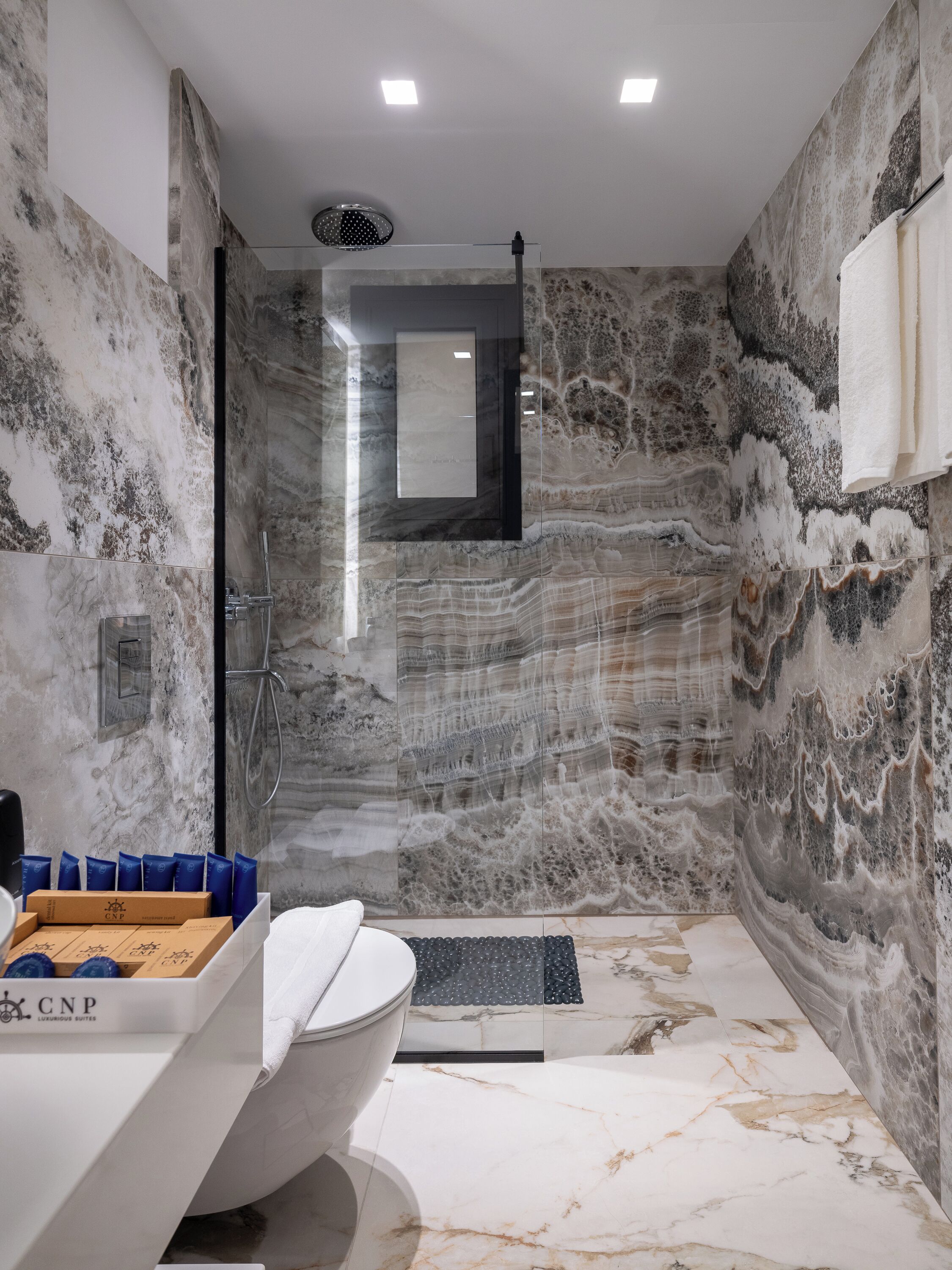 A modern bathroom with a marble wall, a freestanding bathtub, a shower enclosure, and a towel rack.