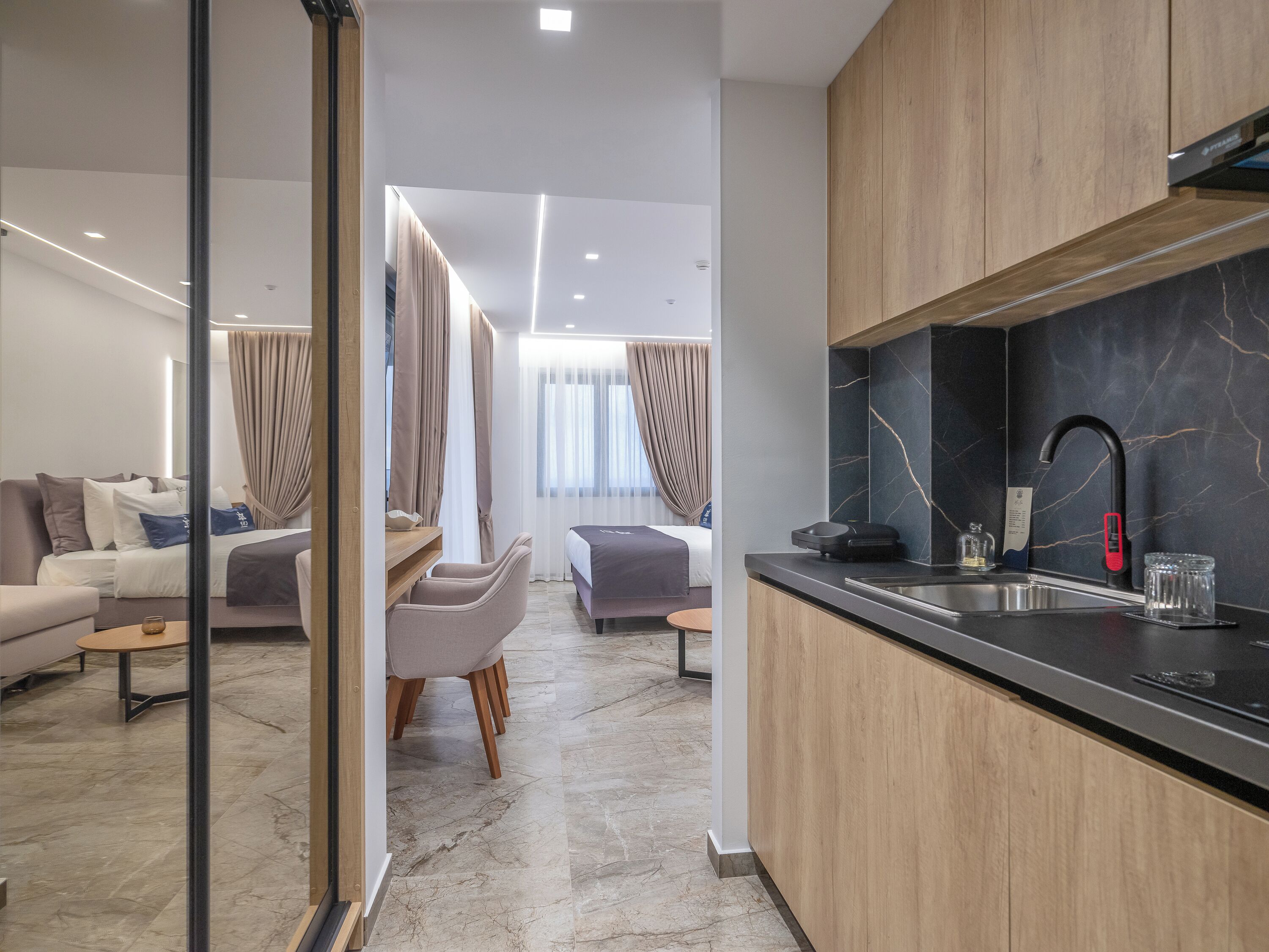 A modern hotel room with a kitchen area, a dining area, and a living room.