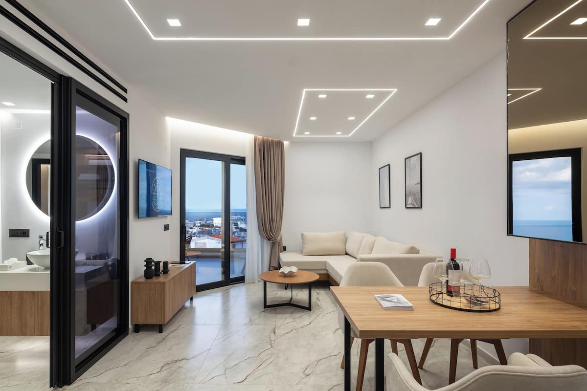 Une chambre d’hôtel moderne dotée d’un balcon, d’un miroir rond, d’un canapé, d’une table à manger et d’un téléviseur.