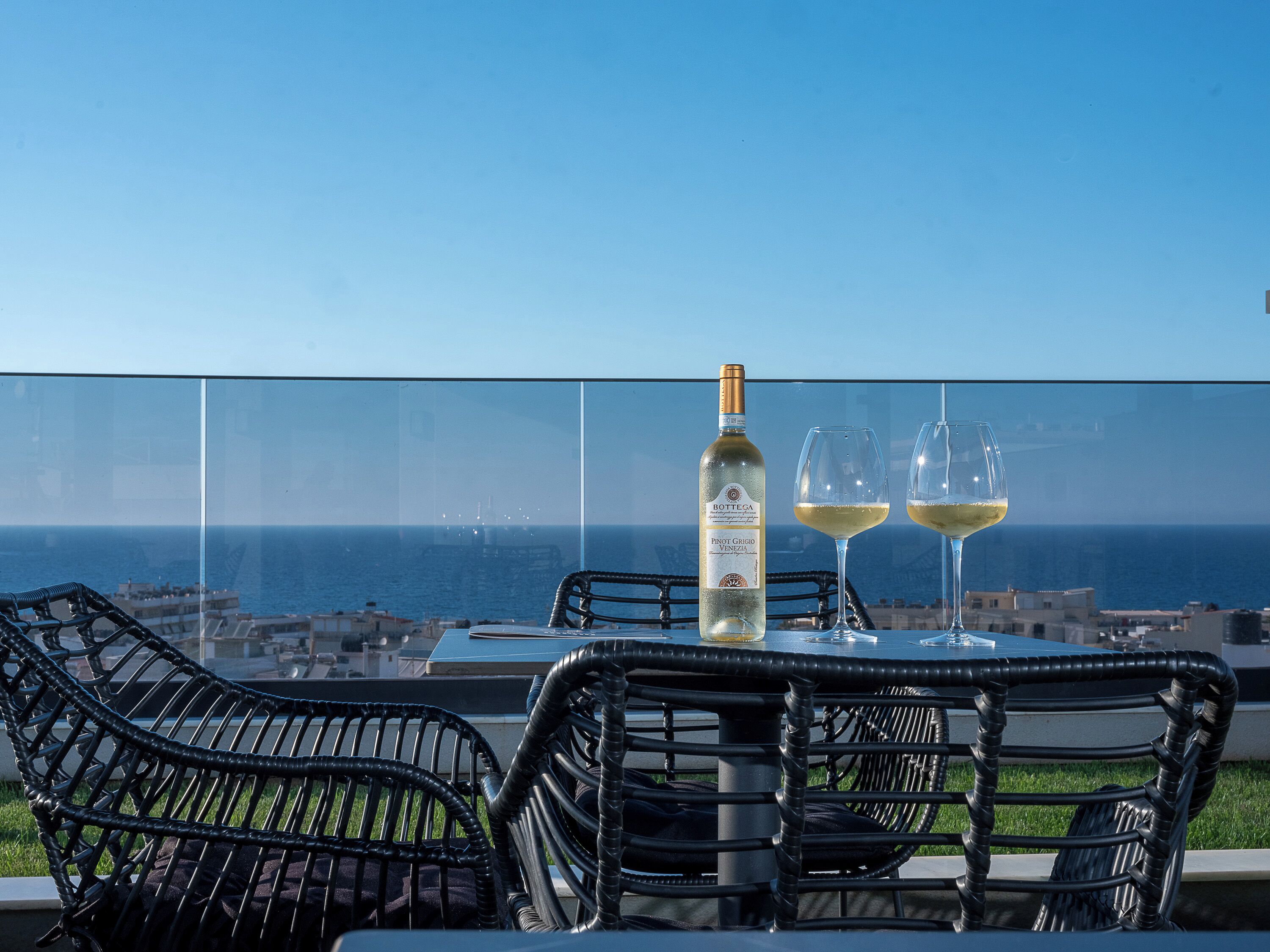 A table with a bottle and two glasses, overlooking a coastal cityscape.