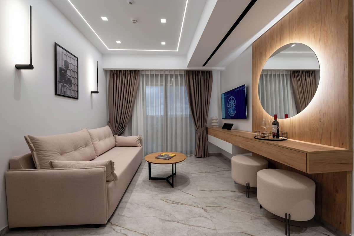 Une chambre d’hôtel moderne, dotée d’un canapé, d’une table basse ronde, d’une coiffeuse en bois avec un miroir et d’une grande fenêtre avec des rideaux.