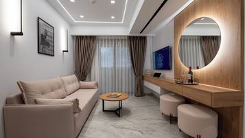 Une chambre d’hôtel moderne, dotée d’un canapé, d’une table basse ronde, d’une coiffeuse en bois avec un miroir et d’une grande fenêtre avec des rideaux.
