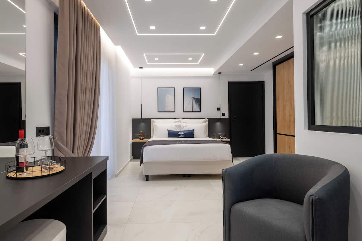 Une chambre d’hôtel moderne avec un lit, un bureau sur lequel se trouvent une bouteille de vin et des verres, une chaise et une grande fenêtre.