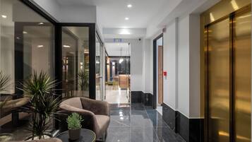 En modern entréhall med en glasvägg, bekväma sittplatser, en krukväxt och ett glänsande marmorgolv.