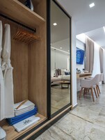A modern hotel room with a wooden wardrobe, a dining area with a table and chairs, and a large mirror reflecting the room.