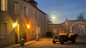 A building with a paved courtyard, a parked vehicle, and a stone wall. - Le Clos du Bas Courtil (Osmanville)