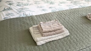 A neatly made bed with a patterned bedspread, pillows with a palm tree design, and a folded blanket on the bed. - Le Clos du Bas Courtil (Osmanville)