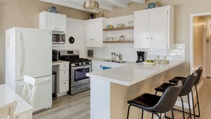 Eine moderne Küche mit weißen Schränken, einer zentralen Kochinsel mit Barhocker, einem eingebauten Backofen und einer Mikrowelle.