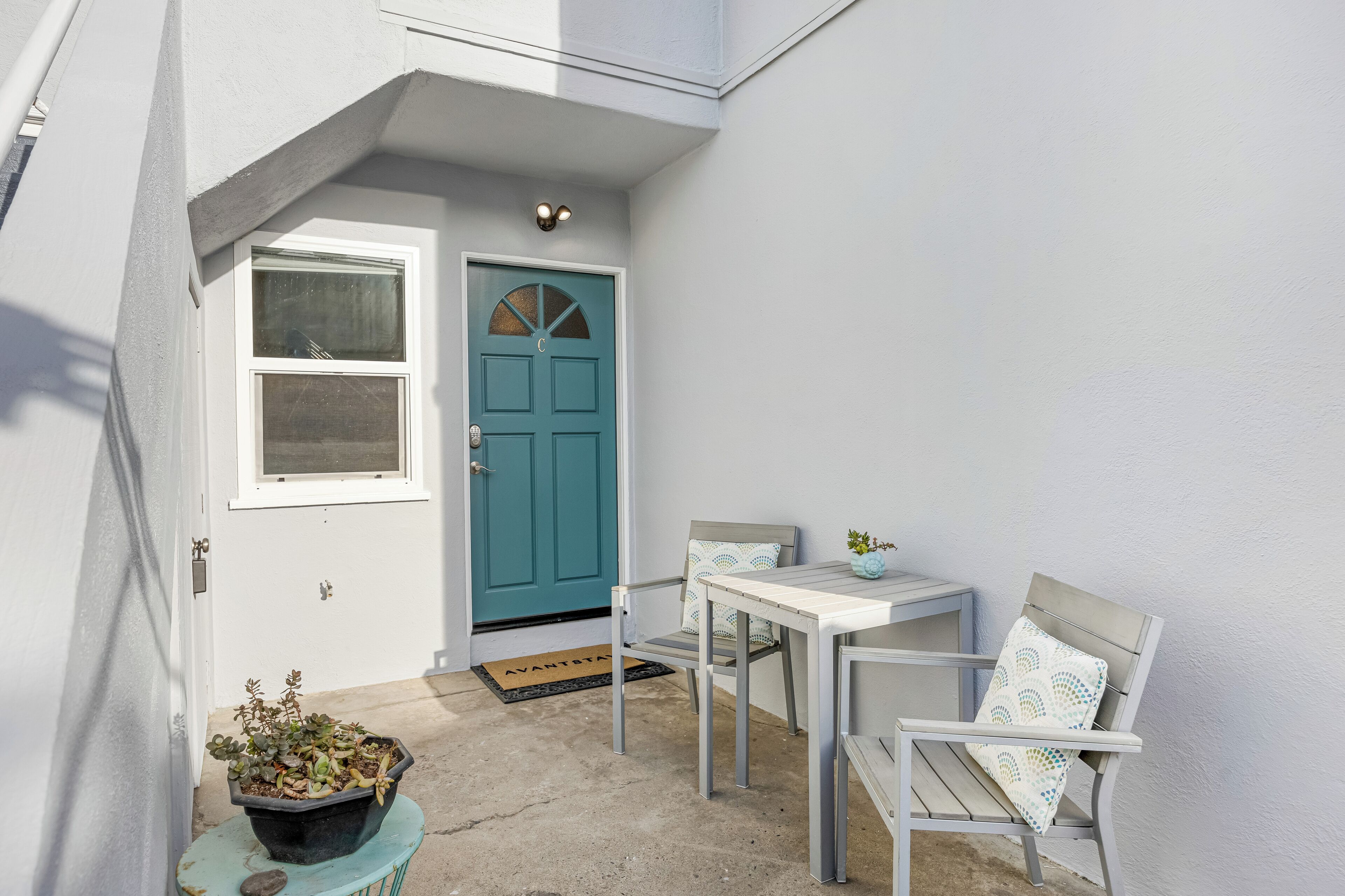 A small outdoor seating area with a teal door, a white table, and two chairs.