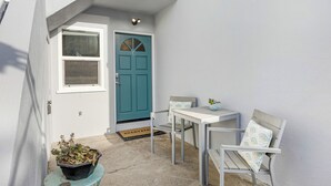 Un pequeño espacio al aire libre con una puerta azul aguamarina, una mesa blanca y dos sillas.