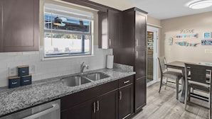 A modern kitchen with dark wood cabinets, granite countertops, a double sink, and a window overlooking a backyard. - PCB Group-Friendly Duplex w/ Pool, Backyard Lounge & 2 Kitchens (Panama City Beach)