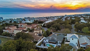 A residential area with houses, a swimming pool, and a view of the ocean at sunset. - PCB Group-Friendly Duplex w/ Pool, Backyard Lounge & 2 Kitchens (Panama City Beach)