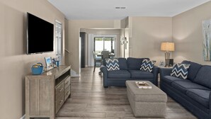 A living room with a sofa set, a TV mounted on the wall, and a wooden cabinet. - PCB Group-Friendly Duplex w/ Pool, Backyard Lounge & 2 Kitchens (Panama City Beach)
