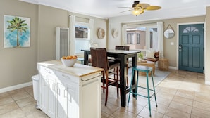 A kitchen with a dining area, white cabinets, a ceiling fan, and a teal door.