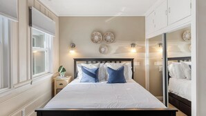 A bedroom with a large bed, bedside tables, a nightstand, wall sconces, and decorative wall art.