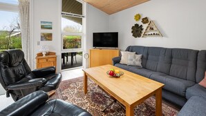 A modern living room with a grey sofa, a wooden coffee table, a black leather chair, and a television on a wooden stand. - "Gertrud" - 950m to the fjord by Interhome (Tarm)