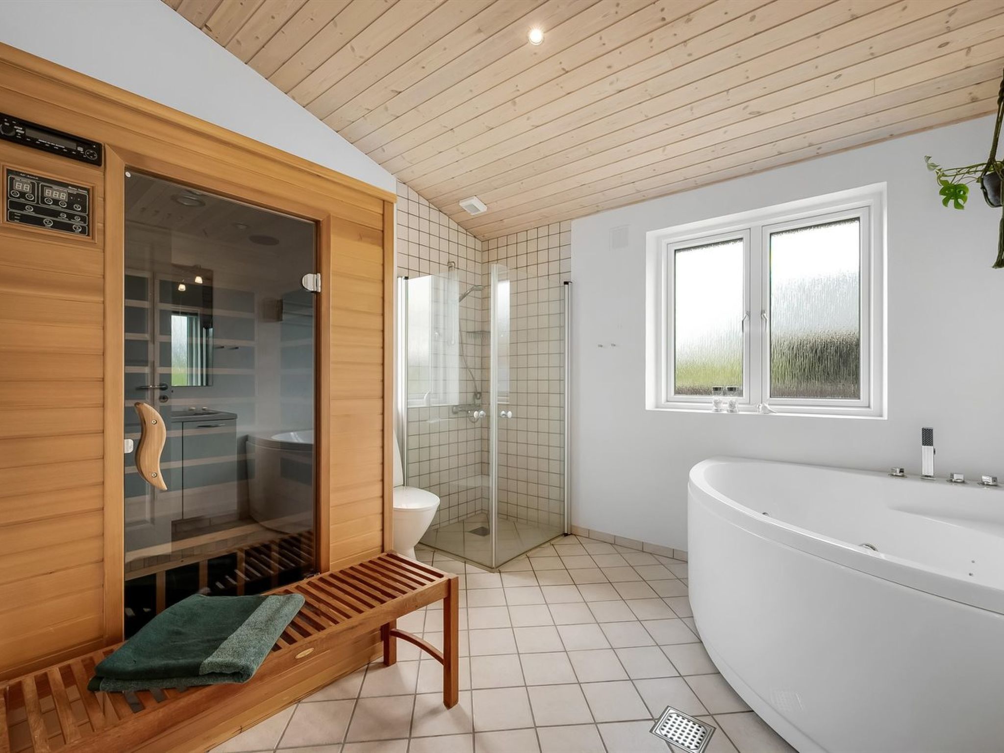 Une salle de bain moderne avec un sauna en bois, une douche à parois de verre, une baignoire sur pieds et une fenêtre laissant entrer la lumière naturelle.