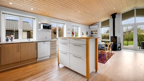 A modern kitchen with wooden flooring, white cabinets, a central island, and a large window overlooking a garden. - "Gertrud" - 950m to the fjord by Interhome (Tarm)